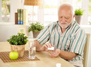 elderly man taking pill at home, sitting at living room table.